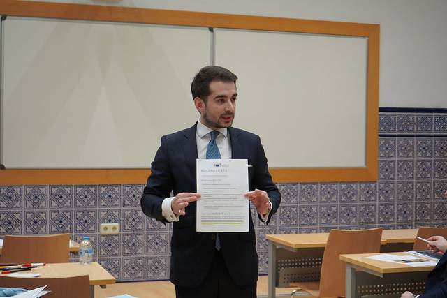 Un hombre vestido de traje sostiene un documento en una sala de reunión.