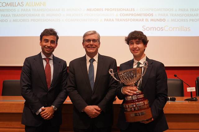 Tres hombres posan sonrientes en un evento, uno de ellos sostiene un trofeo.