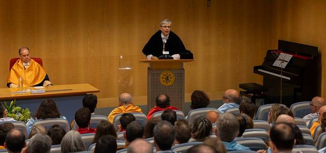 Una ceremonia académica con un orador en el podio y un público atento.