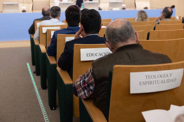 Un grupo de personas sentadas en un auditorio con etiquetas en sus sillas que indican diferentes temas.