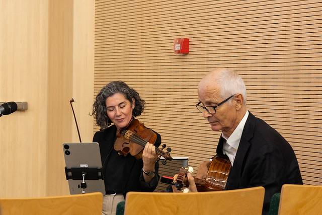 Una mujer toca el violín mientras un hombre acompaña con la guitarra en un ambiente acogedor.