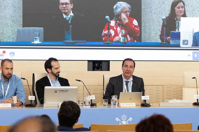 La imagen muestra a un panel de conferenciantes en un evento, con una presentación proyectada detrás de ellos.