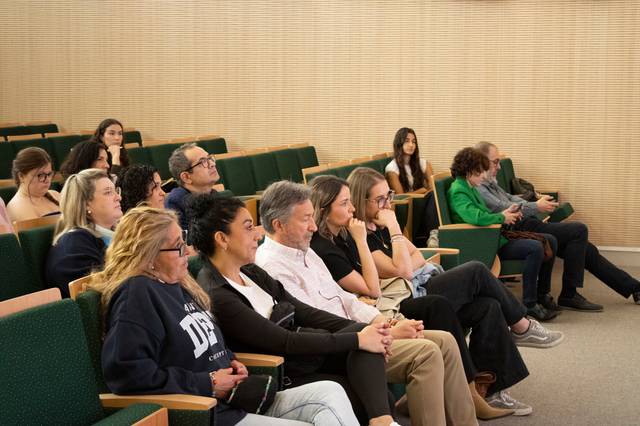 Un grupo de personas sentadas en un auditorio, prestando atención a una presentación.