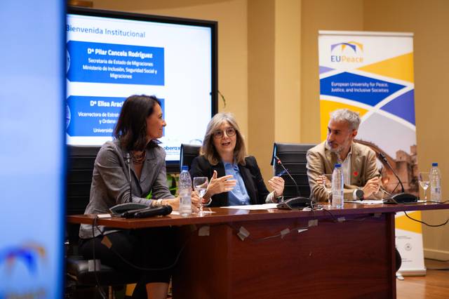 Una mesa redonda en la que participan tres personas discutiendo en un ambiente académico.