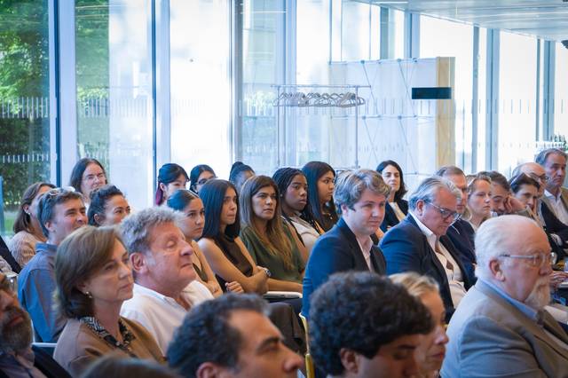 Un grupo de personas atentas durante una conferencia o evento en un salón luminoso.