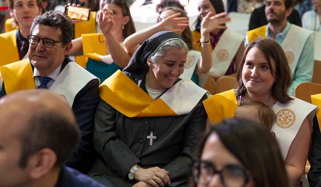 Un grupo de personas sentadas sonrientes, algunas con sashes amarillos, en un evento de celebración.