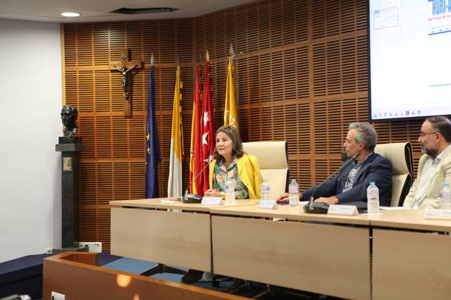Una mesa redonda con panelistas en un auditorio, donde se encuentran banderas y una escultura al fondo.