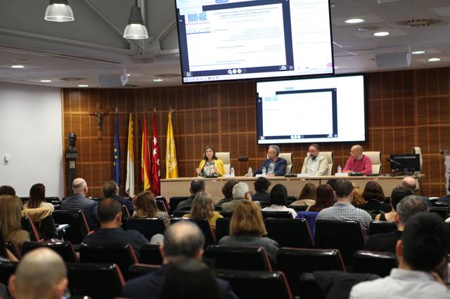 Una conferencia con ponentes en un escenario mientras la audiencia escucha atentamente.
