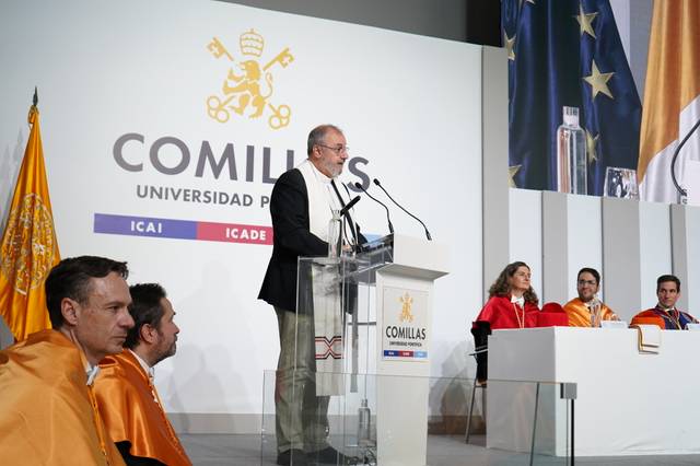 Una ceremonia académica en la Universidad Pontificia Comillas con un orador en el podio y asistentes en la mesa.