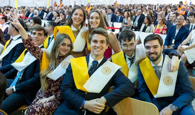 Un grupo de graduados sonríen y posan con sus togas y sashes en una ceremonia de graduación.