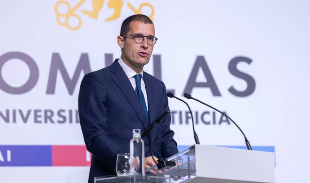 Un hombre con gafas y traje está hablando en un micrófono durante un evento en una universidad.