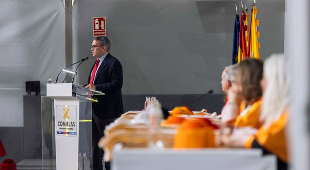 Un orador se dirige a un auditorio en un evento formal con banderas de fondo.