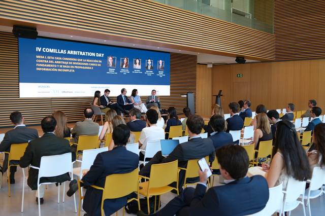 Evento académico sobre arbitraje con panel de expertos y asistentes en un auditorio moderno.