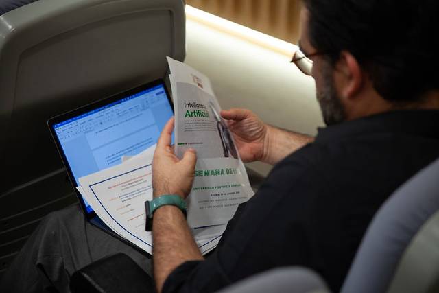 Un hombre revisa documentos sobre Inteligencia Artificial mientras utiliza una computadora portátil.