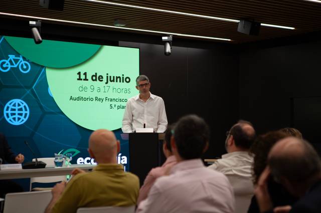 Un hombre habla en un evento mientras varias personas lo escuchan.
