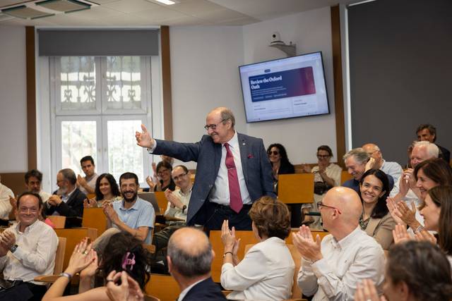 Un hombre en traje se dirige a una audiencia en un salón lleno de gente que aplaude.