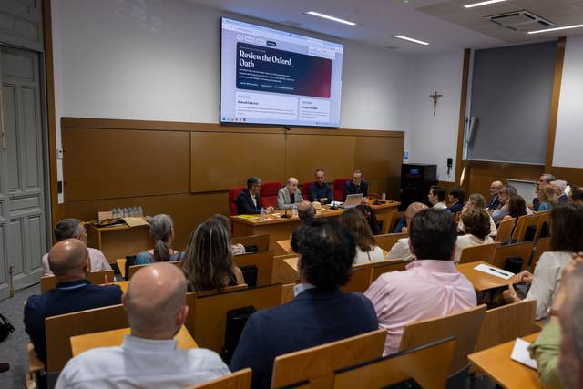 Una conferencia académica con varios ponentes en un auditorio, rodeados de asistentes atentos.