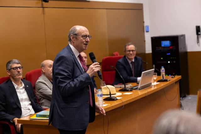 Un grupo de hombres se encuentra en una sala de conferencias, uno de ellos está hablando con un micrófono en mano.