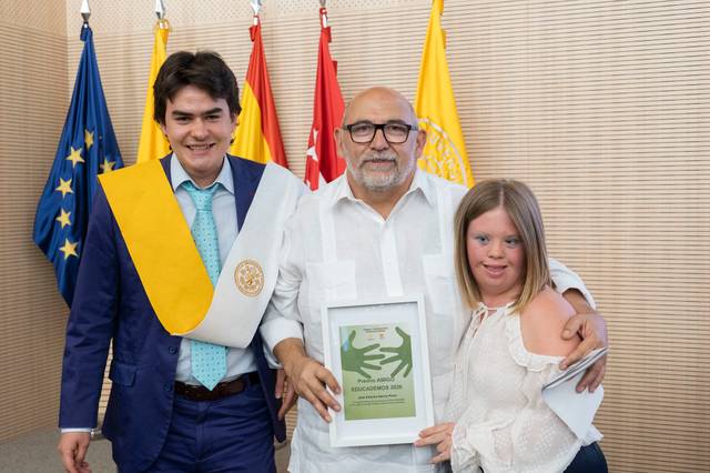 Tres personas posan juntas sosteniendo un premio en un evento formal.