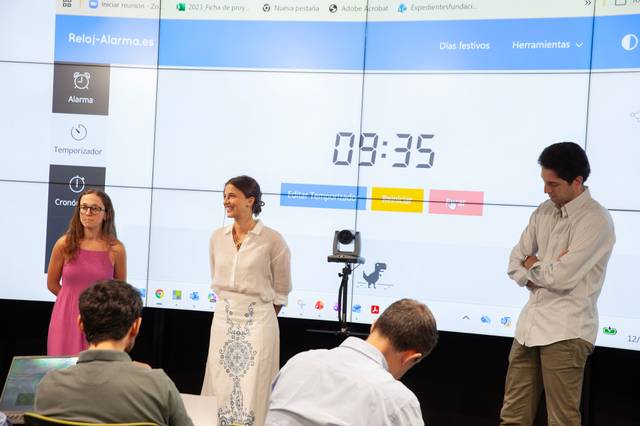 Tres personas están presentando una actividad frente a una pantalla con un cronómetro visible.