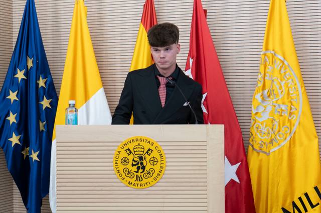 Un joven de pie frente a un podio iluminado, rodeado de banderas de diferentes países.
