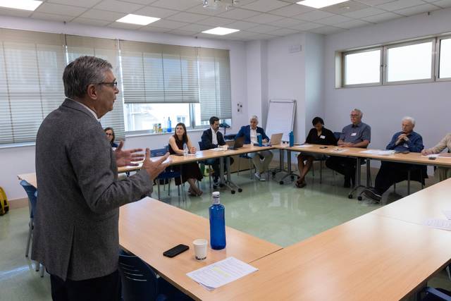 Una reunión con varias personas sentadas alrededor de una mesa mientras un hombre habla.