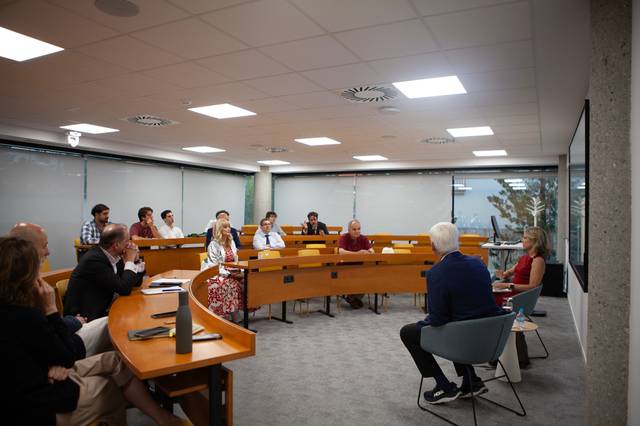 Una reunión en una sala con varias personas sentadas alrededor de una mesa en forma de U.