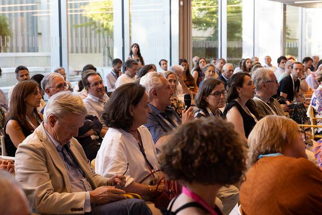 Una multitud de personas sentadas en un evento o conferencia, prestando atención a un ponente.