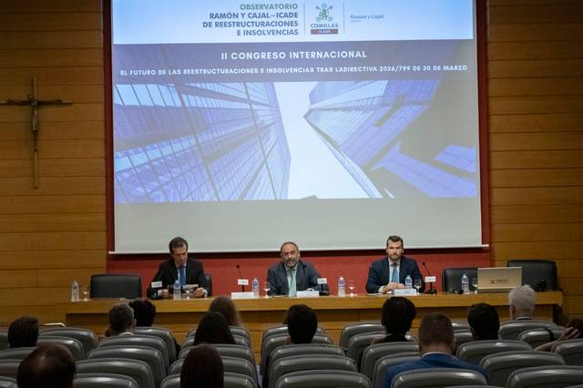 Fotografía de un congreso internacional sobre reestructuraciones e insolvencias, con ponentes en el escenario y una audiencia en el fondo.