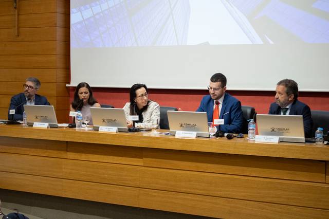 La imagen muestra a un grupo de personas sentadas en una mesa durante un evento o conferencia.