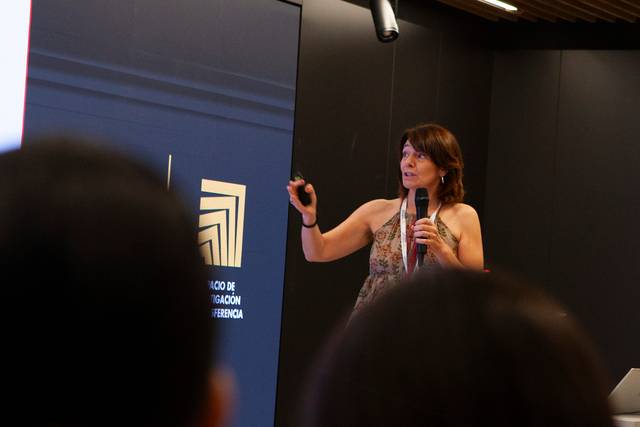 Una mujer presenta en una sala de conferencias mientras es observada por el público.