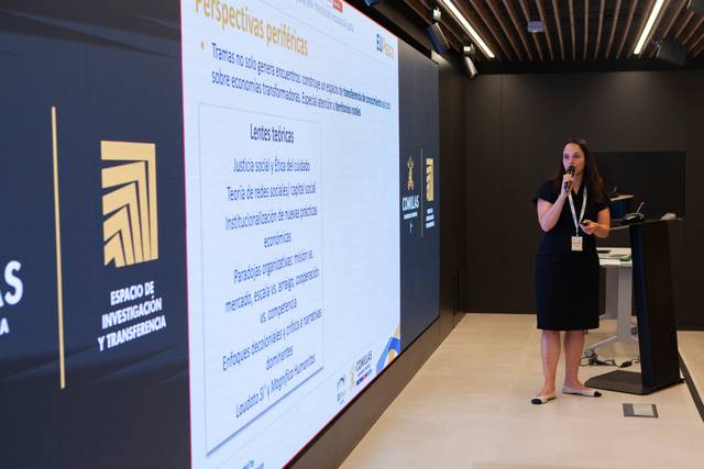 Una mujer presenta información en una pantalla grande durante un evento académico.