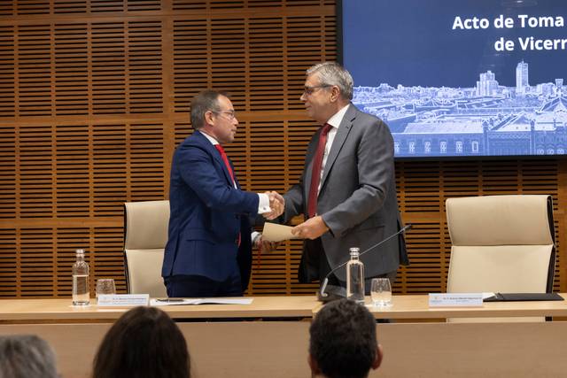 Dos hombres se dan la mano durante un acto formal en un entorno institucional.