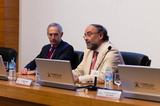 Dos hombres sentados en un panel de discusión con computadoras portátiles frente a ellos.