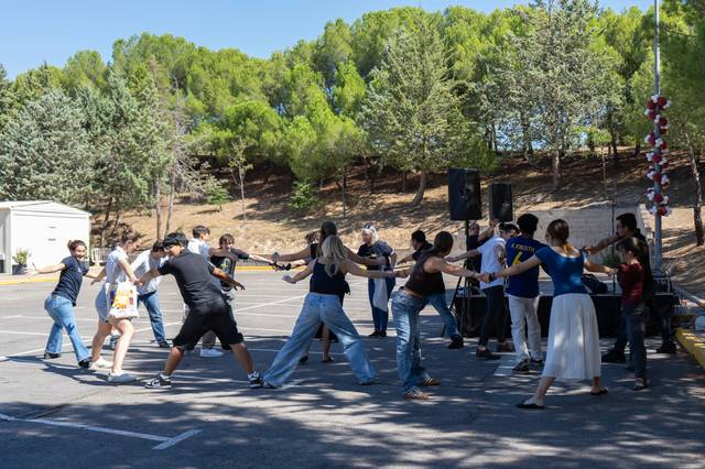 Un grupo de personas está participando en una actividad al aire libre, sosteniéndose de las manos en un ambiente festivo.