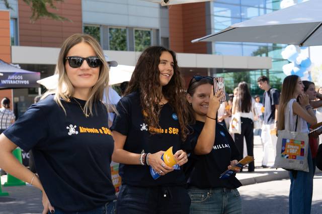 Tres jóvenes sonrientes con camisetas oscuras participan en un evento al aire libre.