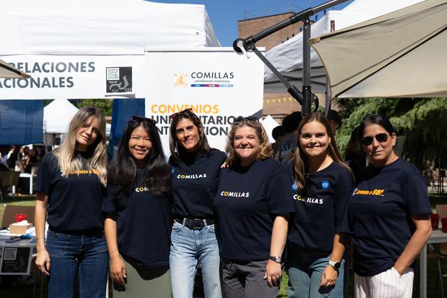 Grupo de mujeres sonriendo en un evento al aire libre, vistiendo camisetas con el logotipo de Comillas.