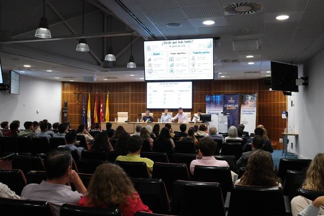 Una conferencia con un panel de ponentes y un público atento en un ambiente académico.