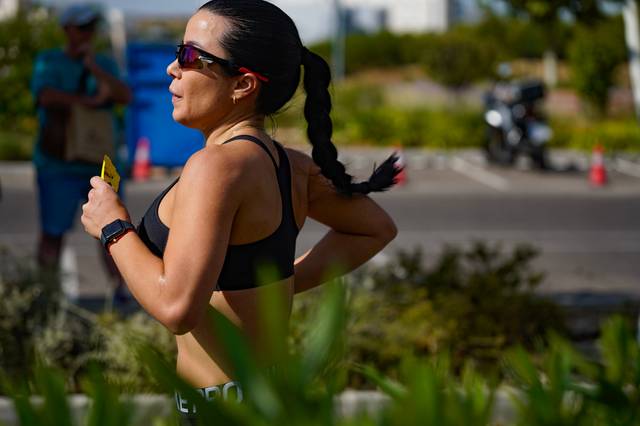 Una mujer corre al aire libre mientras lleva lentes de sol y una camiseta sin mangas.