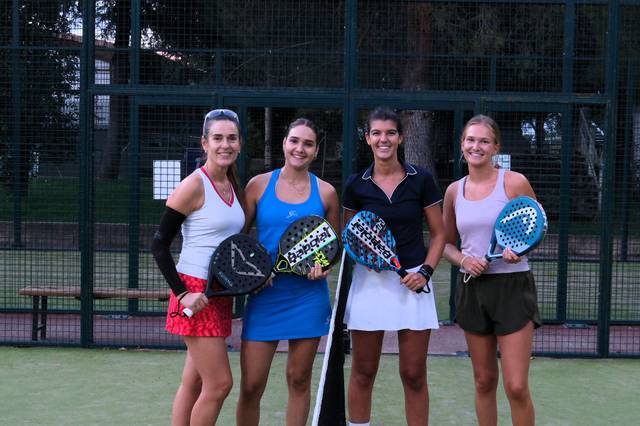 Cuatro mujeres posando juntas con palas de pádel en una cancha al aire libre.