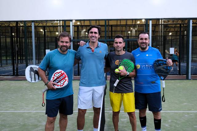 Cuatro hombres posan juntos en una cancha de pádel, sosteniendo palas y pelotas.