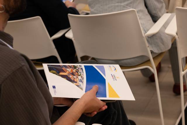 Una persona sostiene un folleto al asistir a un evento en un ambiente interior.
