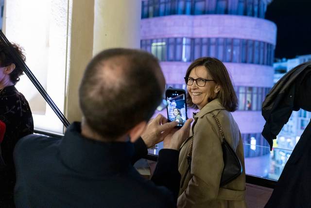 Una mujer sonriente está posando para una foto tomada por otra persona en un entorno iluminado por la noche.