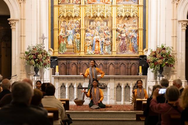 Un grupo de bailarinas se presenta en un escenario frente a un público en una iglesia decorada con arte religioso.