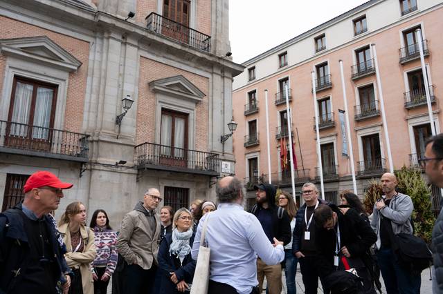 Un grupo de personas está escuchando a un guía turístico frente a un edificio en una plaza.
