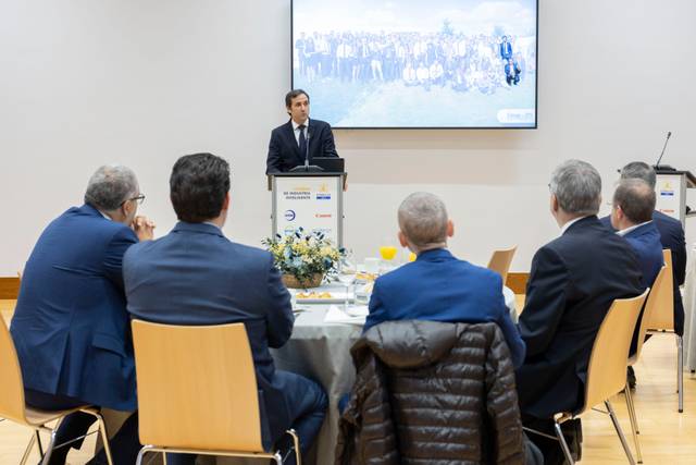 Un hombre está hablando frente a un grupo de personas sentadas alrededor de una mesa en un evento.