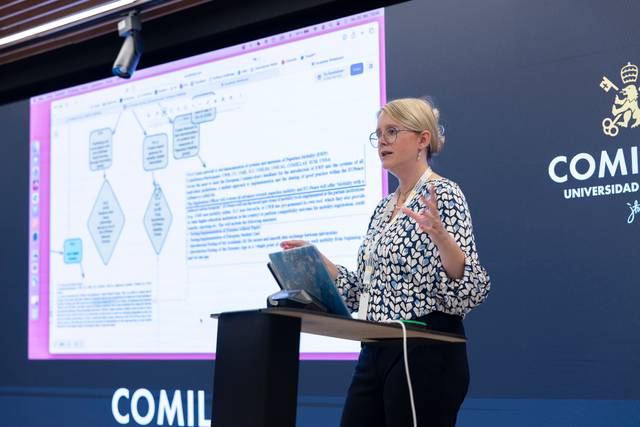 Una mujer está presentando información en una pantalla mientras se dirige a una audiencia en un entorno académico.