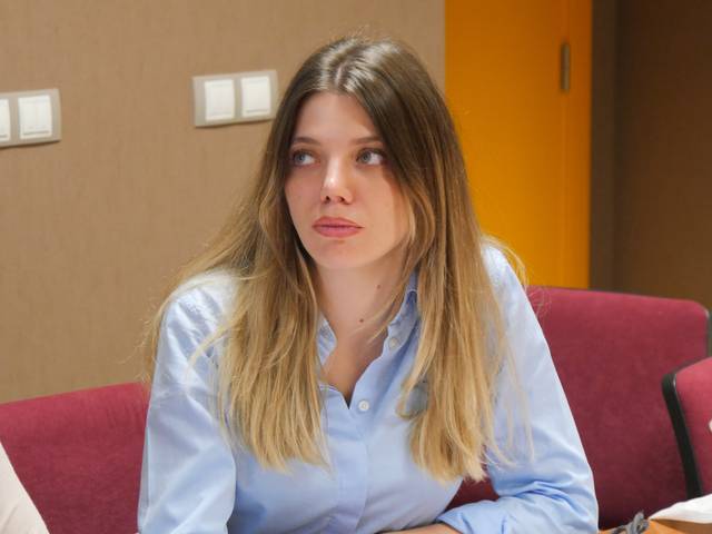 Una joven con cabello largo y rubio mira hacia un lado mientras está sentada en una reunión.