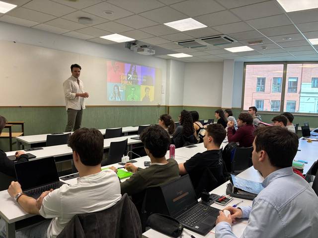 Un profesor está impartiendo una clase a un grupo de estudiantes en un aula moderna.