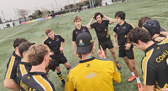 Un grupo de jóvenes jugadores de rugby escucha atentamente las instrucciones de su entrenador en un campo.